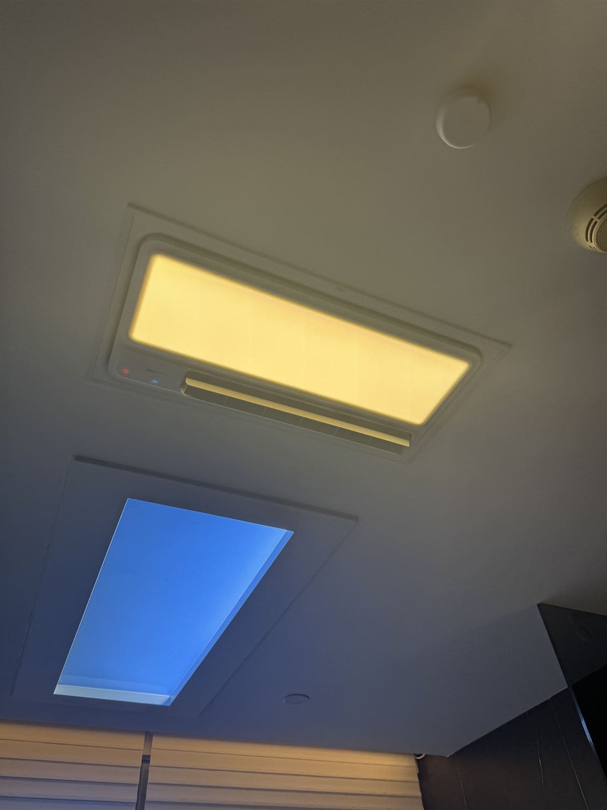 A recessed ceiling light panel demonstrating tunable colour — one section glowing warm amber, an adjacent panel cool daylight blue