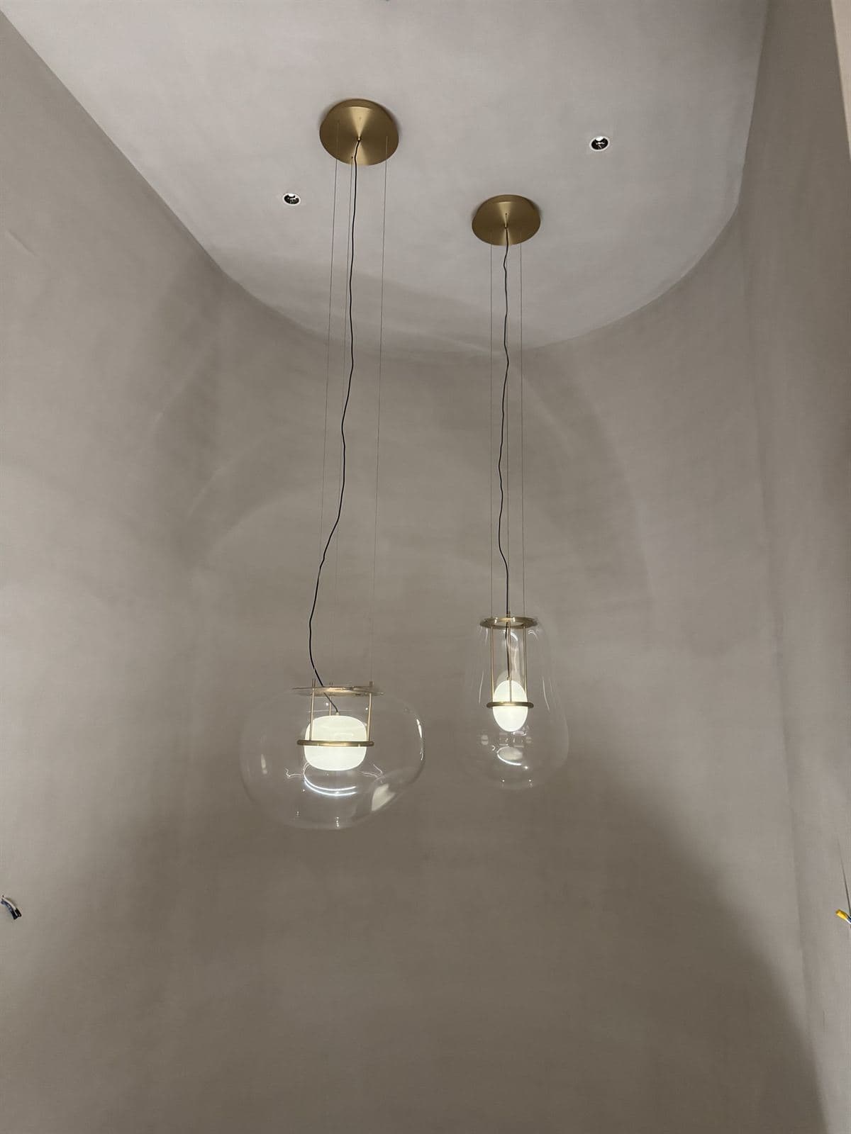 Two clear-glass GUOCIO Rise pendant lights with internal white diffusers and brass accents hanging from a pale curved ceiling