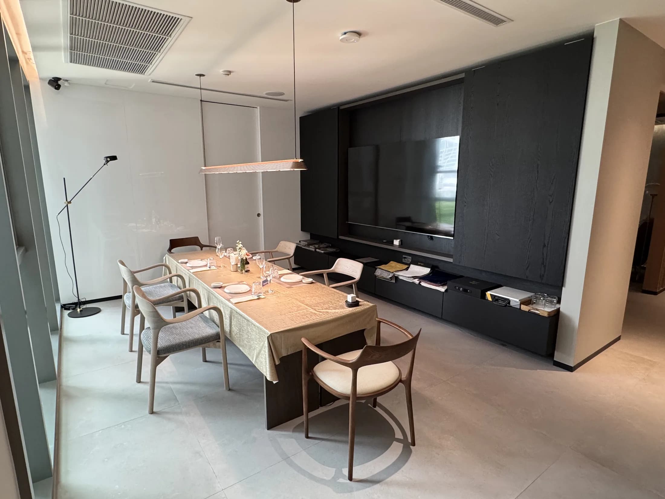 Dining table with designer chairs beside a dark walnut media wall in the showroom